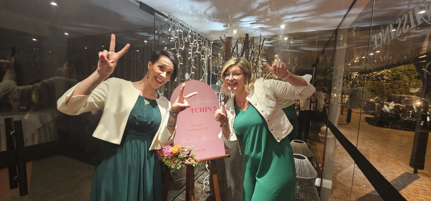 Deux complices brandissent le panneau d'accueil d'un mariage pendant la soirée